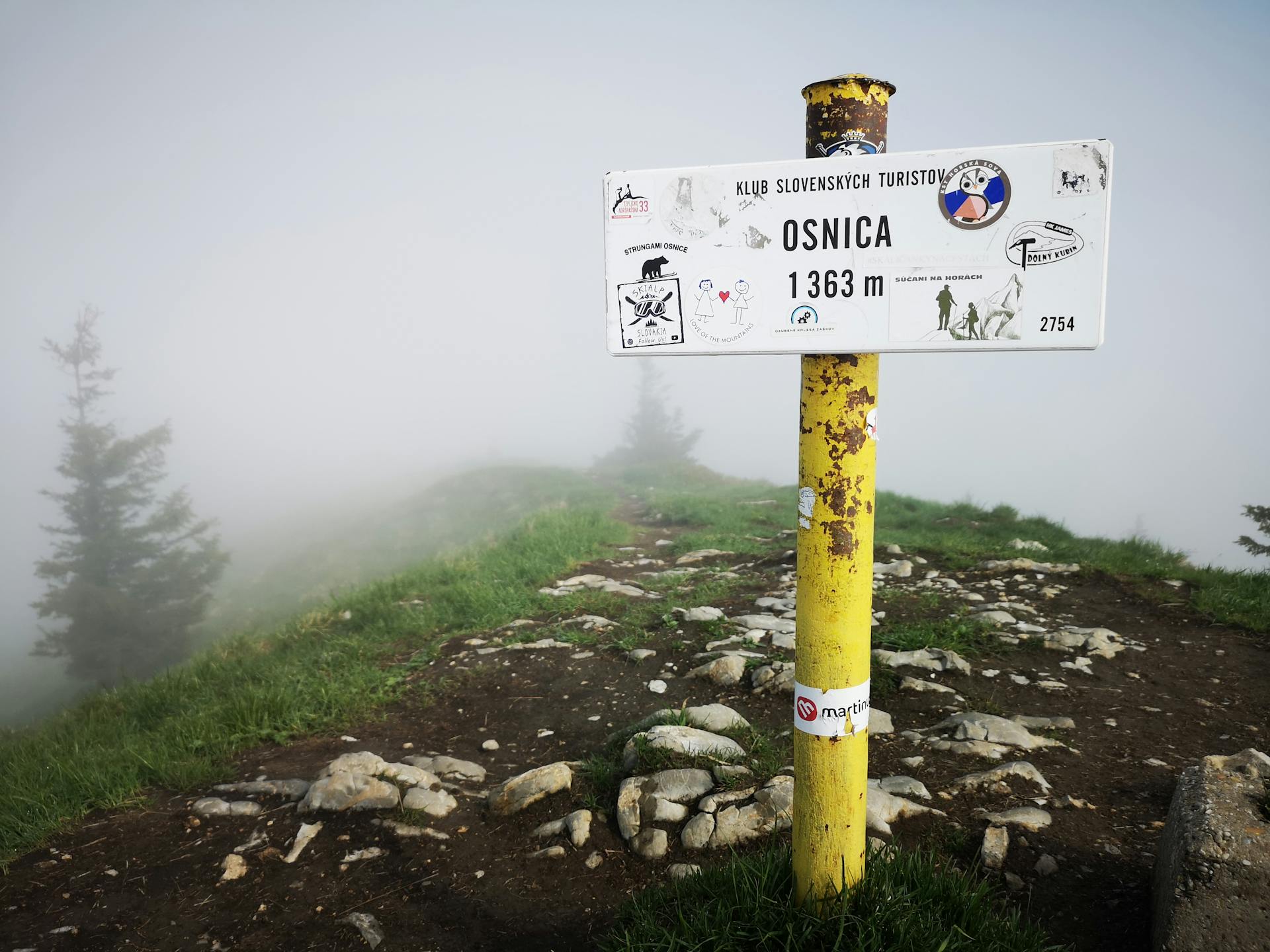 Mountain trail signpost at Osnica peak in foggy weather, showcasing nature's tranquility.