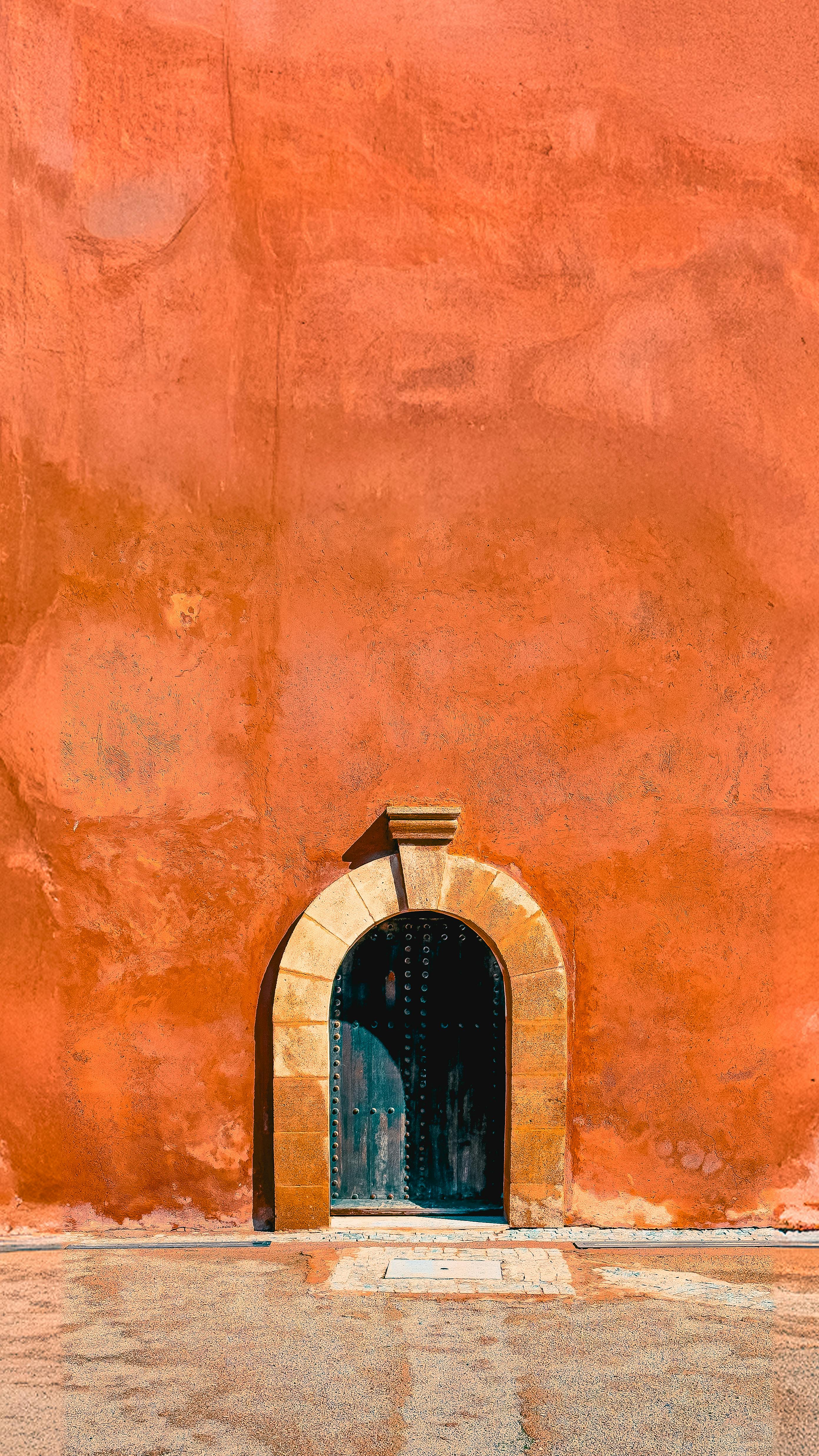 Capture of a vibrant orange wall with a classic arched doorway in Morocco.