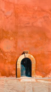Capture of a vibrant orange wall with a classic arched doorway in Morocco.