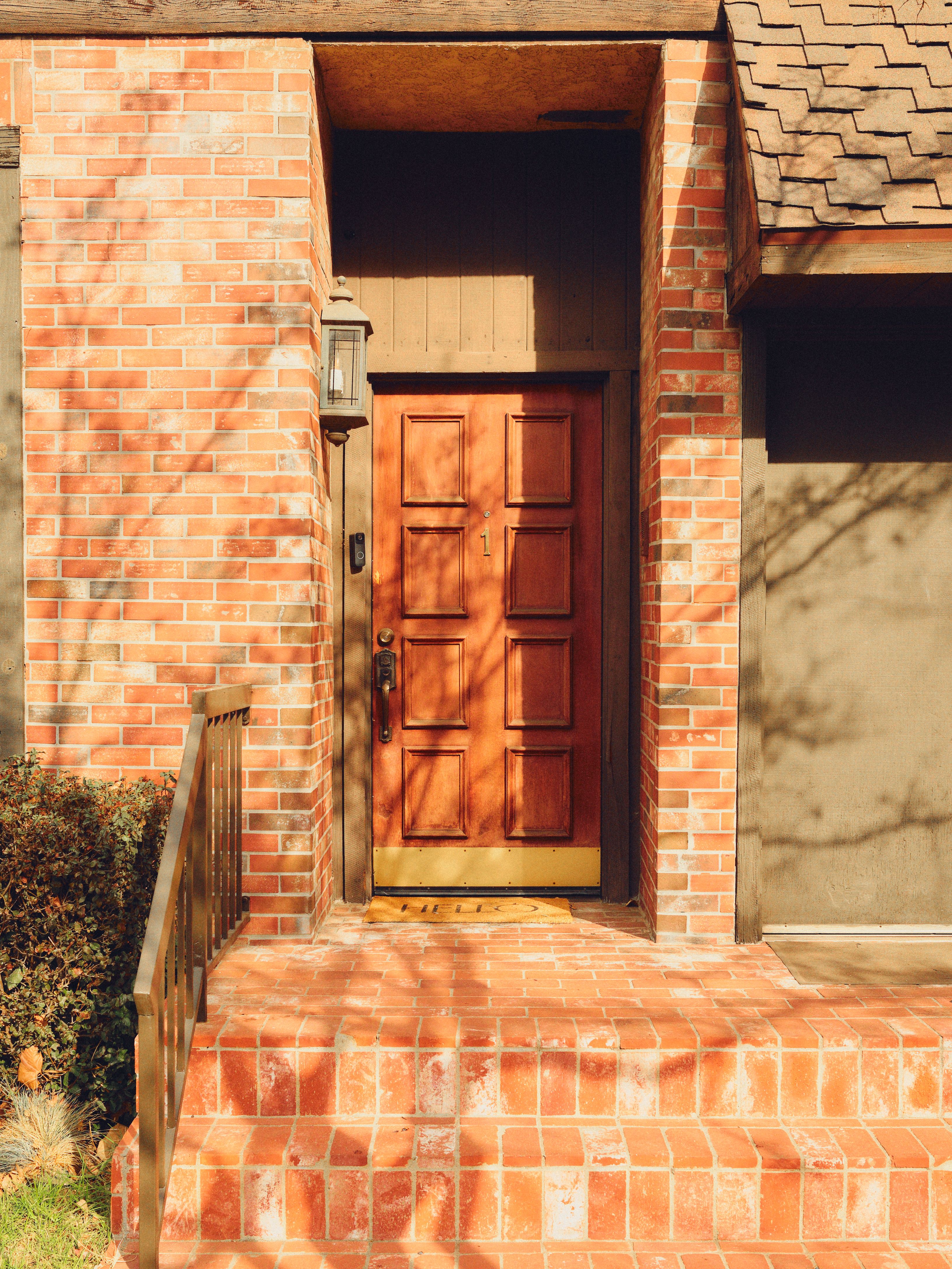 Cozy brick entrance featuring a warm wooden door and classic lantern lighting in a sunlit setting.