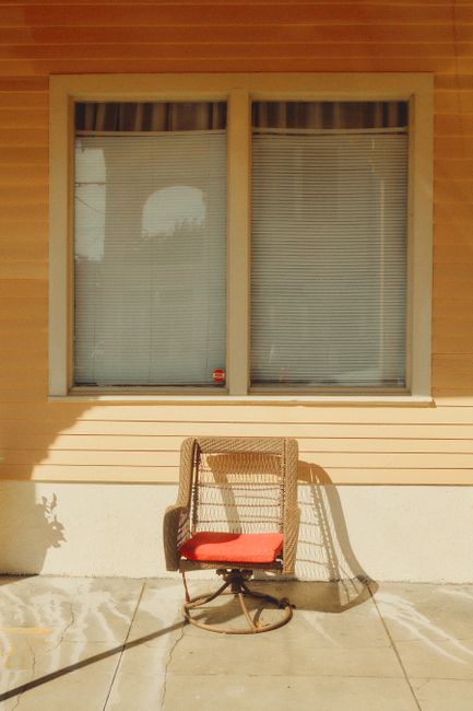 A wicker chair with a red cushion on a sunny New Orleans porch casting long shadows.