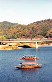 Elegant traditional wooden boats glide on a tranquil Japanese river surrounded by lush hills.