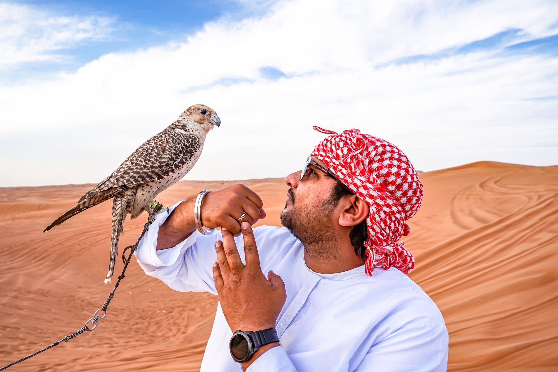 Man interacts with a falcon in the vast Arabian desert showcasing culture and nature.