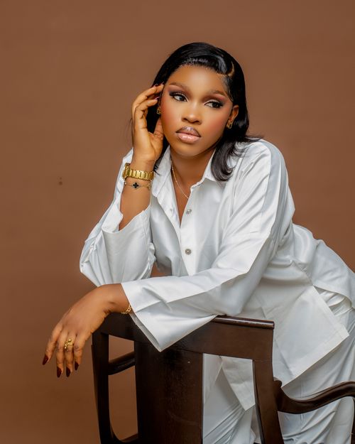 Free Sophisticated woman wearing white shirt poses stylishly indoors against a brown background. Stock Photo