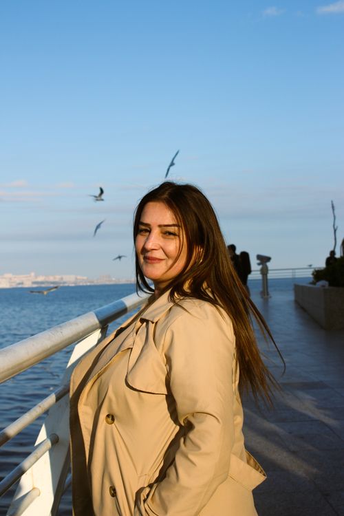 Free Woman in a trench coat enjoying the scenic waterfront in Baku, Azerbaijan during the day. Stock Photo