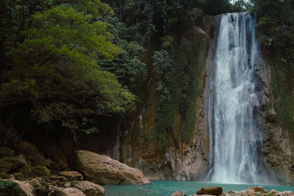 A tranquil waterfall cascades into a turquoise pool surrounded by lush greenery.