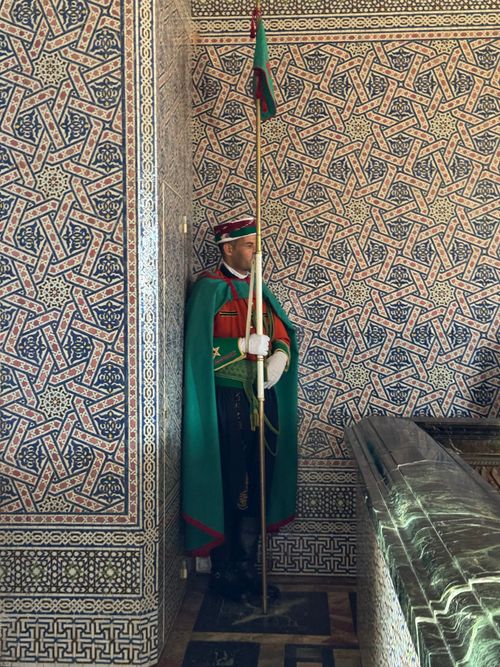 Free A traditional guard in vibrant attire stands in a Moroccan mausoleum, showcasing intricate Islamic architecture. Stock Photo