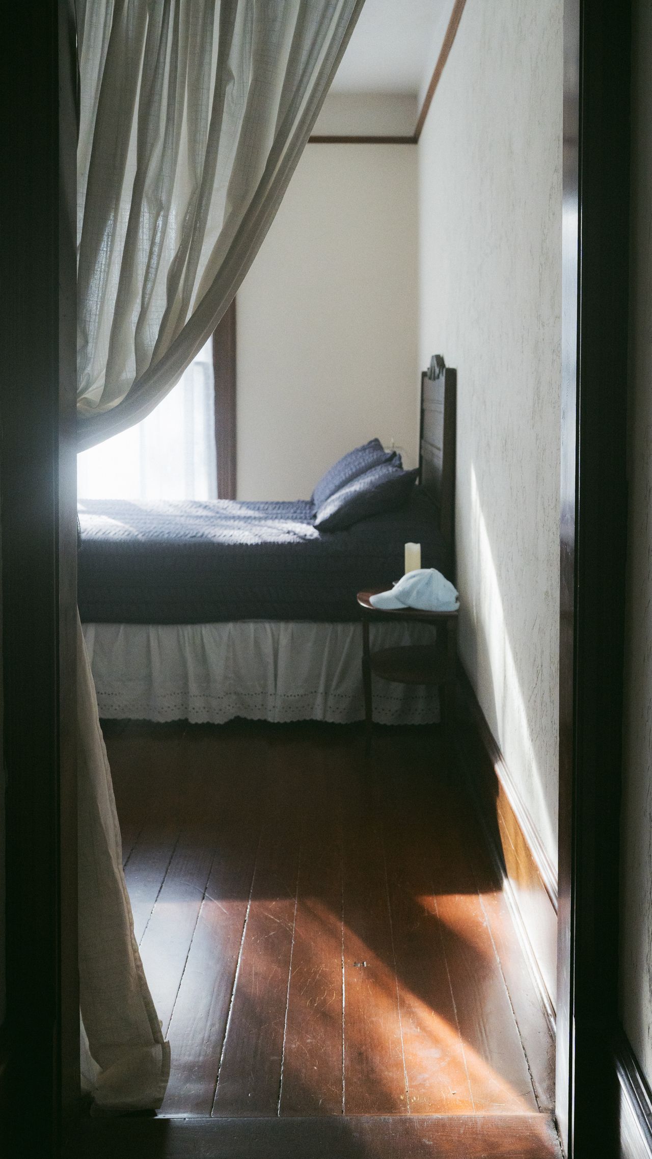 Sunlit bedroom with soft drapes and a dark wood floor