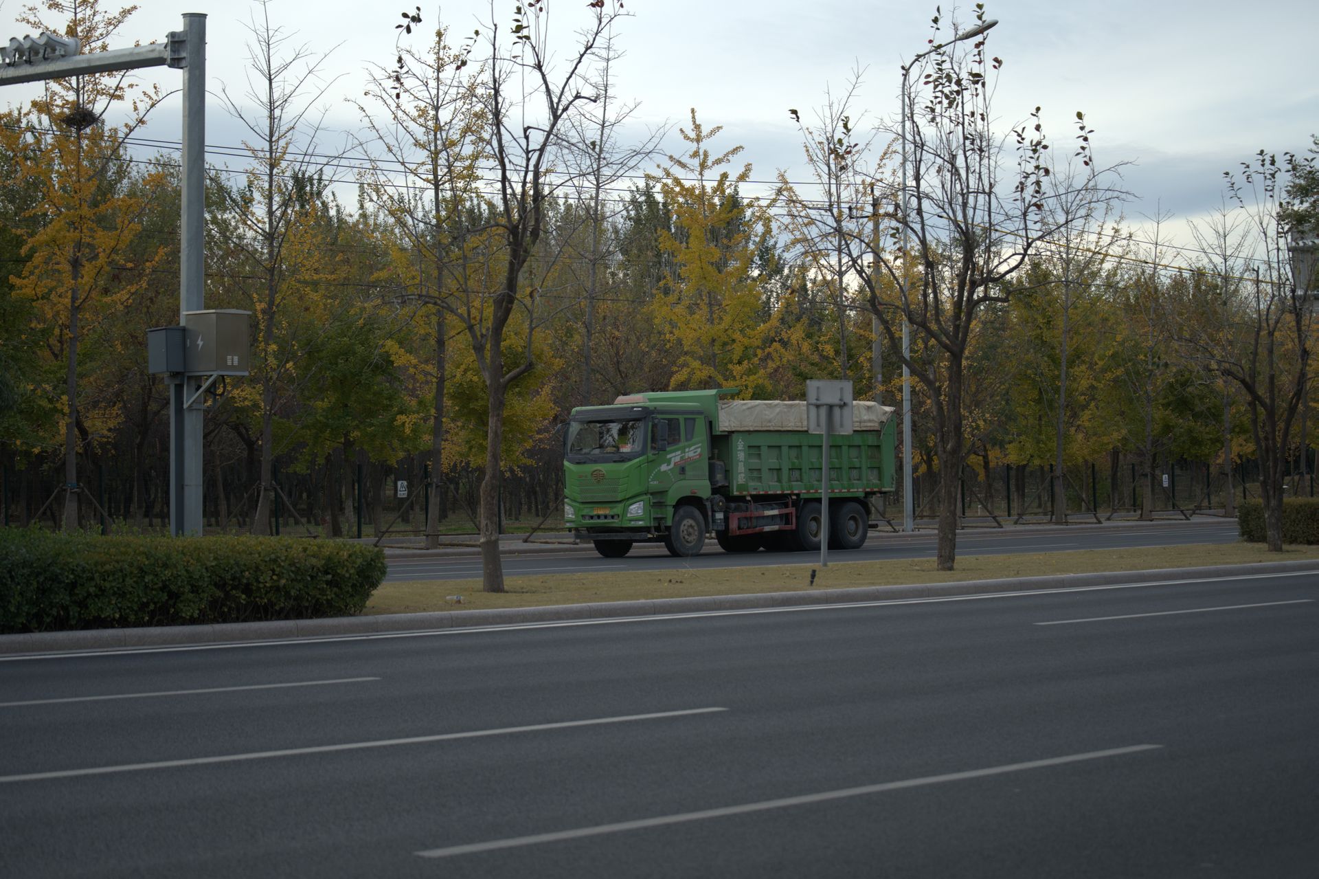 Green truck driving along a tree-lined road in an autumn setting with fall foliage.