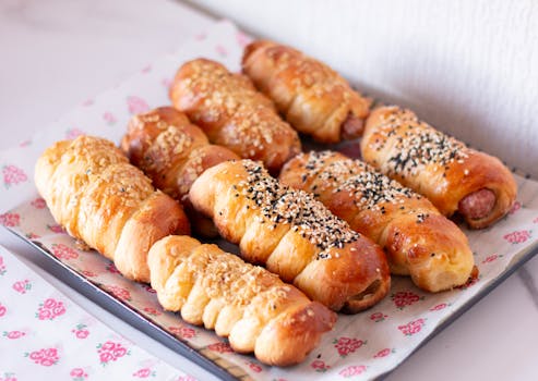 A tray of freshly baked sausage rolls with sesame seed toppings, perfect for a snack or breakfast.