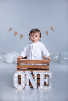 Cute baby standing in a crate with balloons and ONE sign for first birthday.