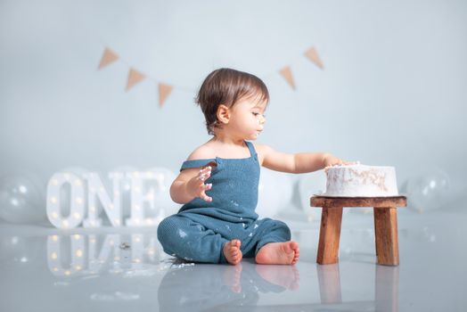 A cute baby celebrates their first birthday with a cake smash in a pastel-themed setup.