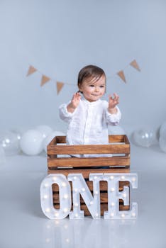 Adorable baby celebrating first birthday with decorative lights and balloons indoors.