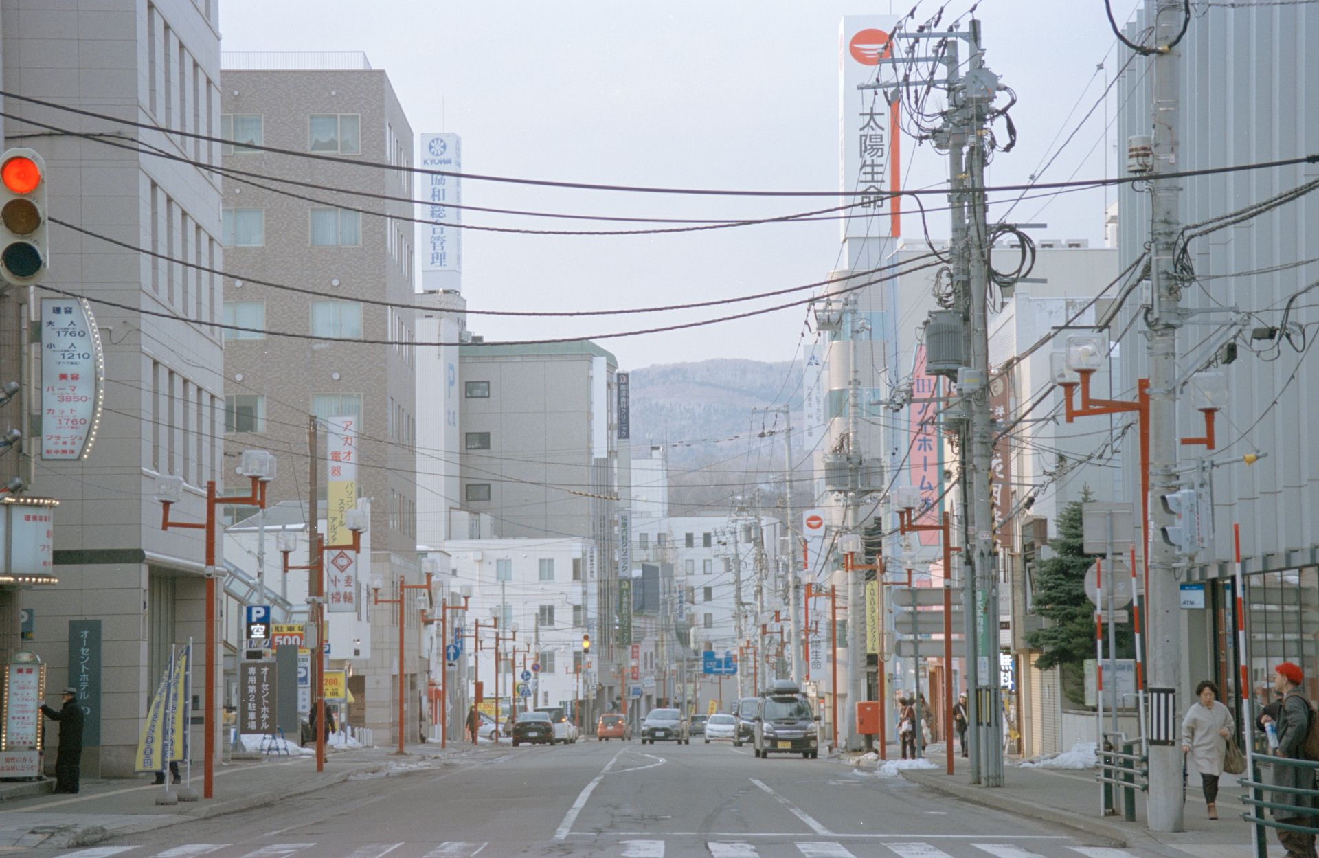 Daytime view of a busy street in a Japanese city with buildings and power lines.
