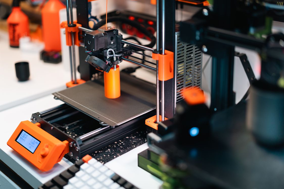 Orange FDM 3D printer actively printing a part on its build plate