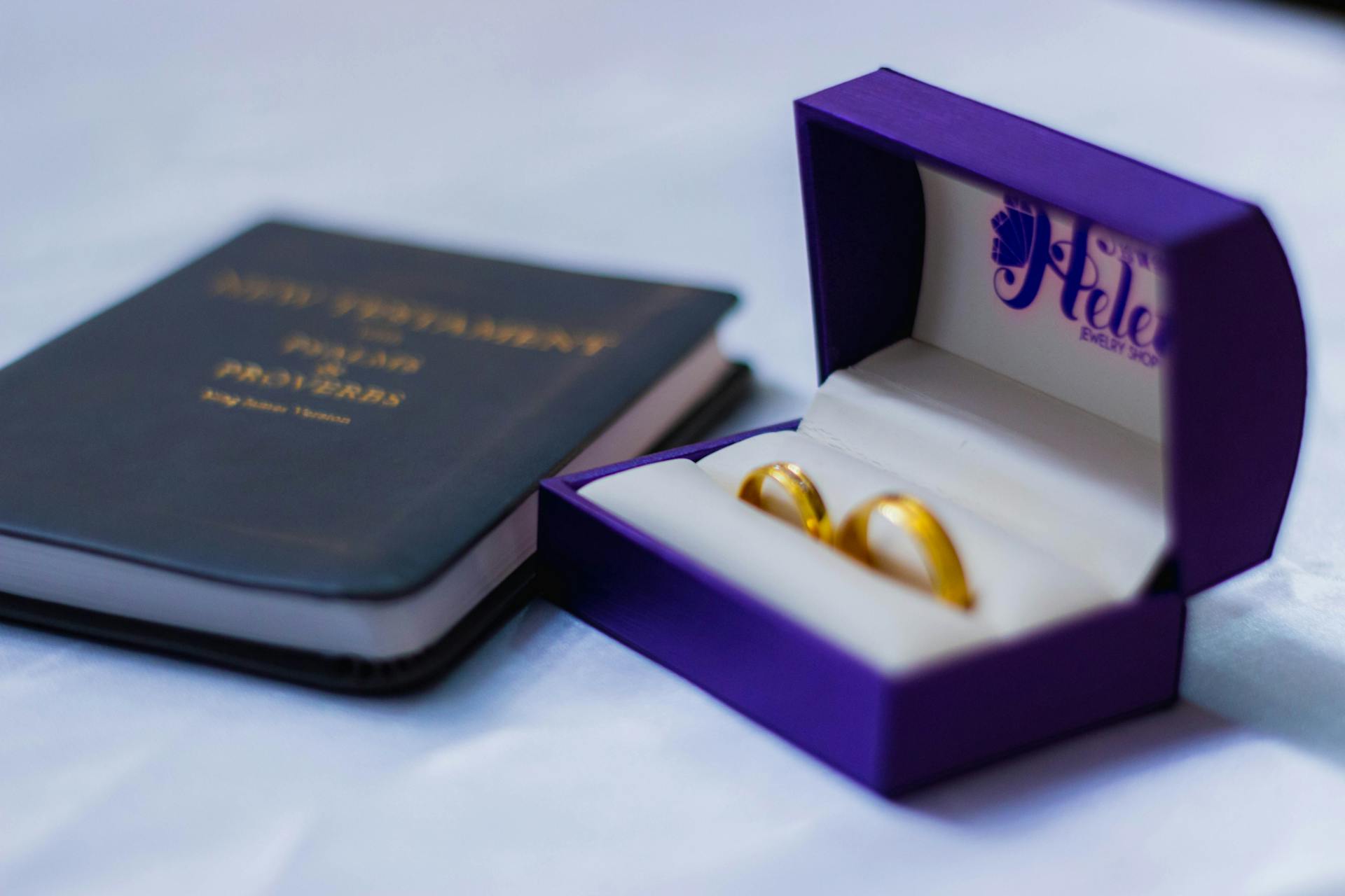 Beautiful gold wedding rings in a purple box beside a New Testament Bible, representing marriage and faith.