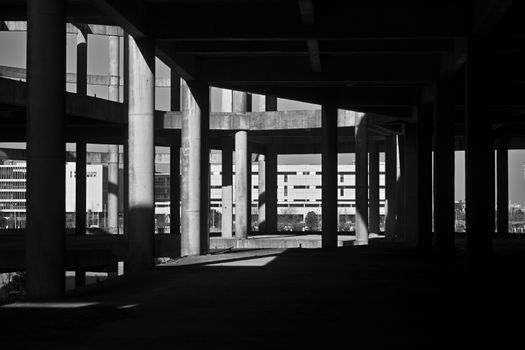 A dramatic black and white photo highlighting shadows and concrete columns under an urban overpass.