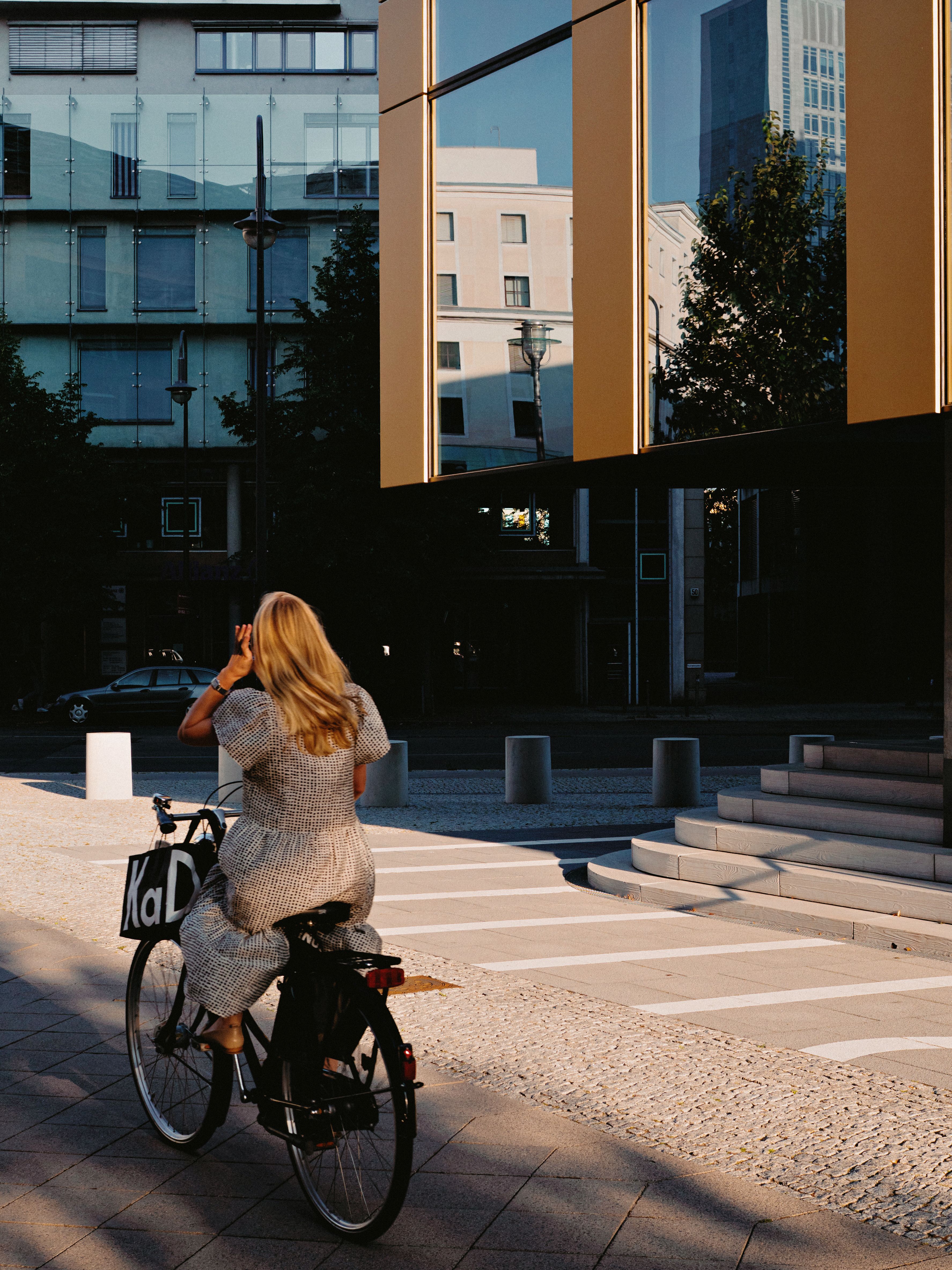 A woman cycles through a modern urban area in Berlin, capturing the evening light and city reflections.