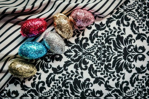 Free Vibrant Easter eggs with glitter on black and white patterned fabric, creating a festive celebration look. Stock Photo