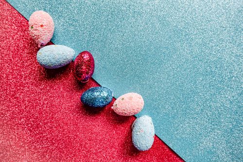 Free Vibrant Easter eggs on a glittery red and blue background creating a festive holiday scene. Stock Photo