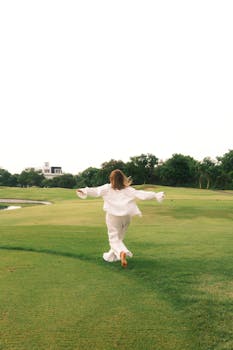 Woman in white running across lush green field, embracing freedom and joy.