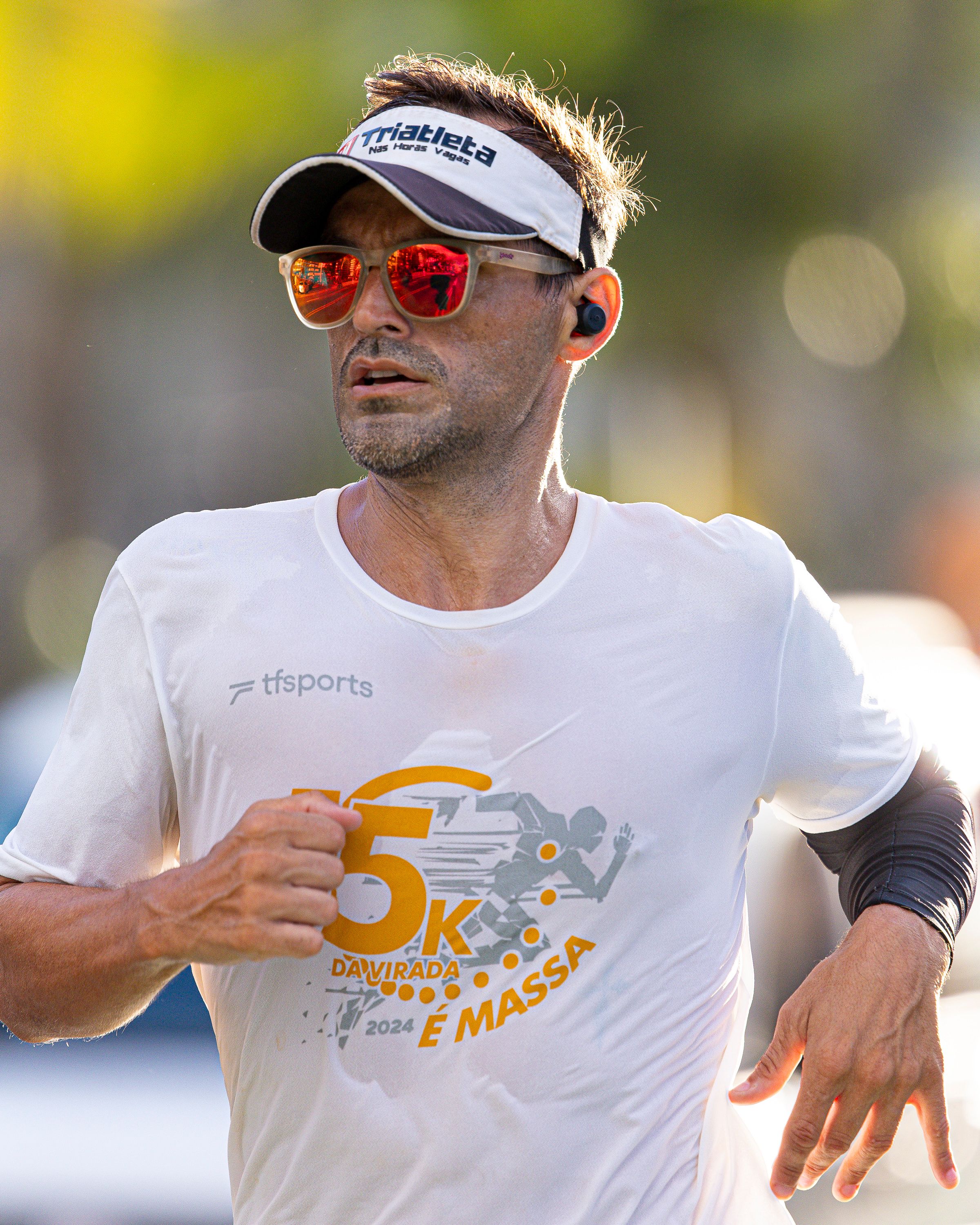 Male runner wearing sunglasses and visor in a 5K race, outdoors in daylight.