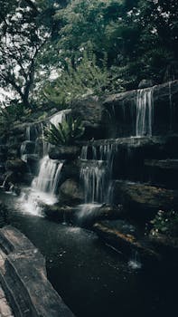 A tranquil waterfall cascading over rocks surrounded by lush greenery in a peaceful forest setting.