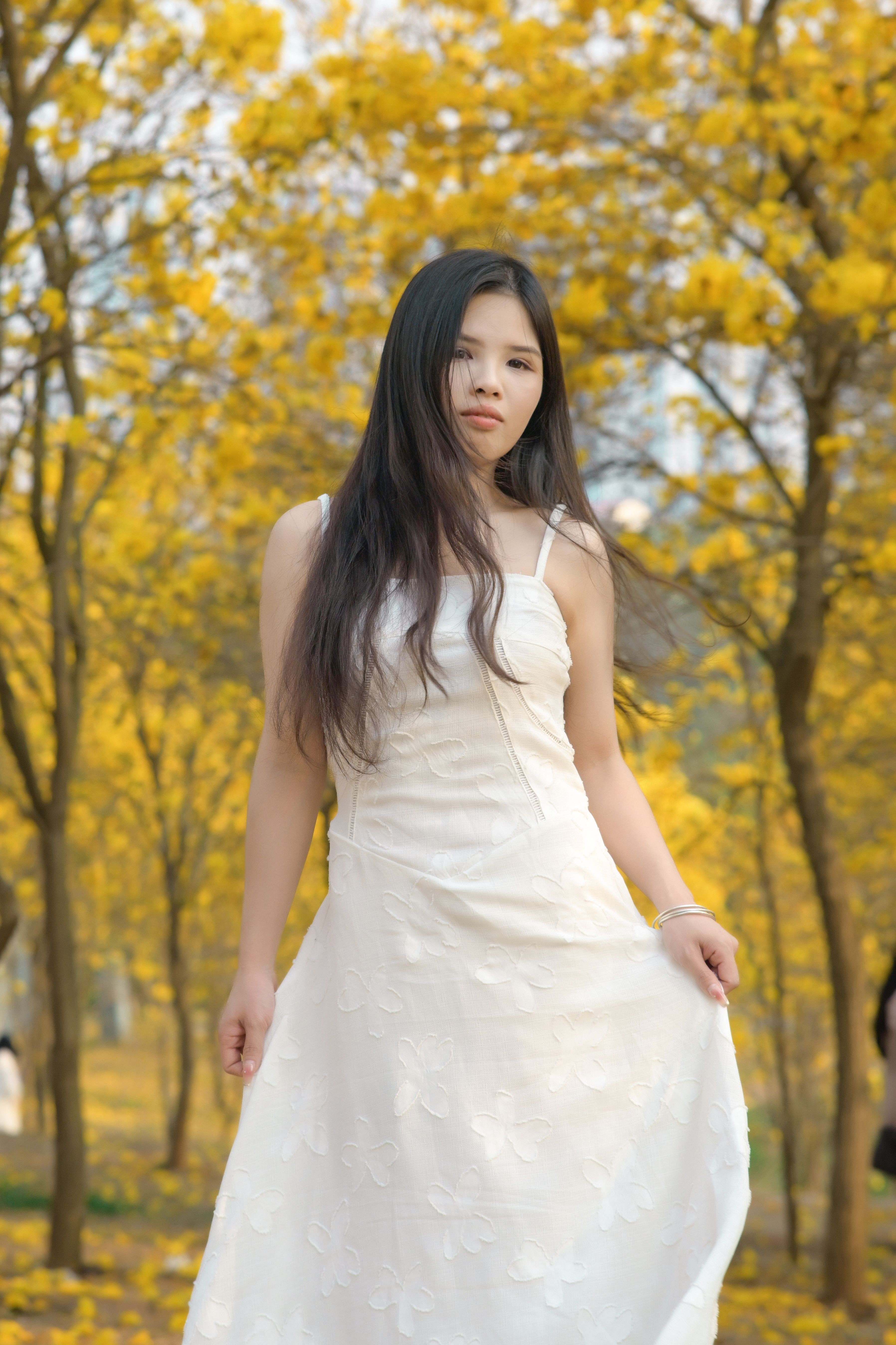 A woman in a white dress stands elegantly among golden autumn trees, embodying natural beauty.