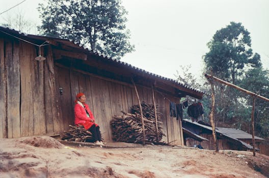 A serene rural scene featuring a woman resting outside a wooden house in the highlands, showcasing traditional life.