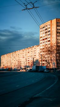 Tall apartment building in city at sunset with empty street and dramatic sky.