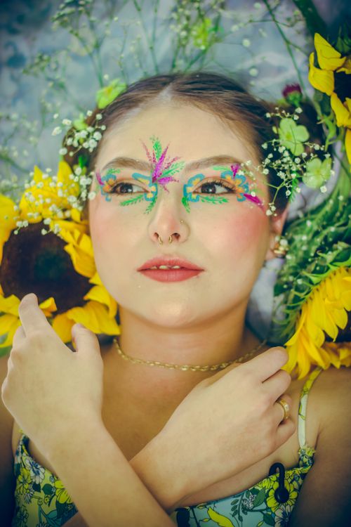 Free Woman with vibrant floral makeup surrounded by sunflowers, showcasing artistic expression. Stock Photo
