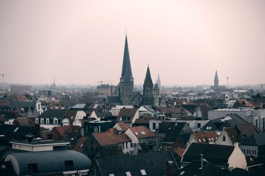 Explore Ghent's charming skyline with iconic Gothic architecture, steeples, and historical buildings against a hazy morning sky.