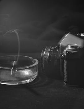 A nostalgic black and white scene with a vintage camera and smoking ashtray evoking a classic mood.