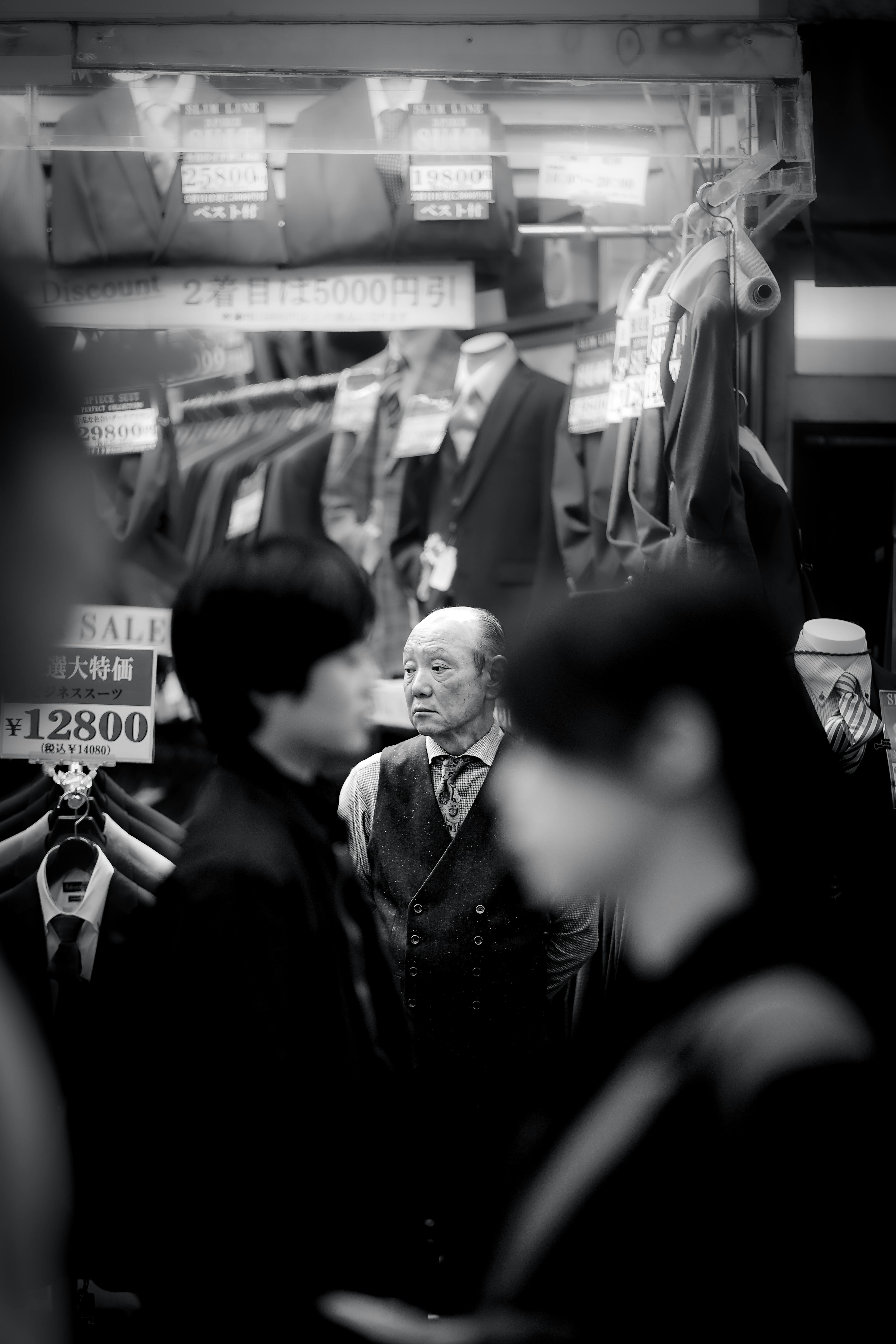 Moody black and white scene of an elderly man in front of an Osaka clothing shop.