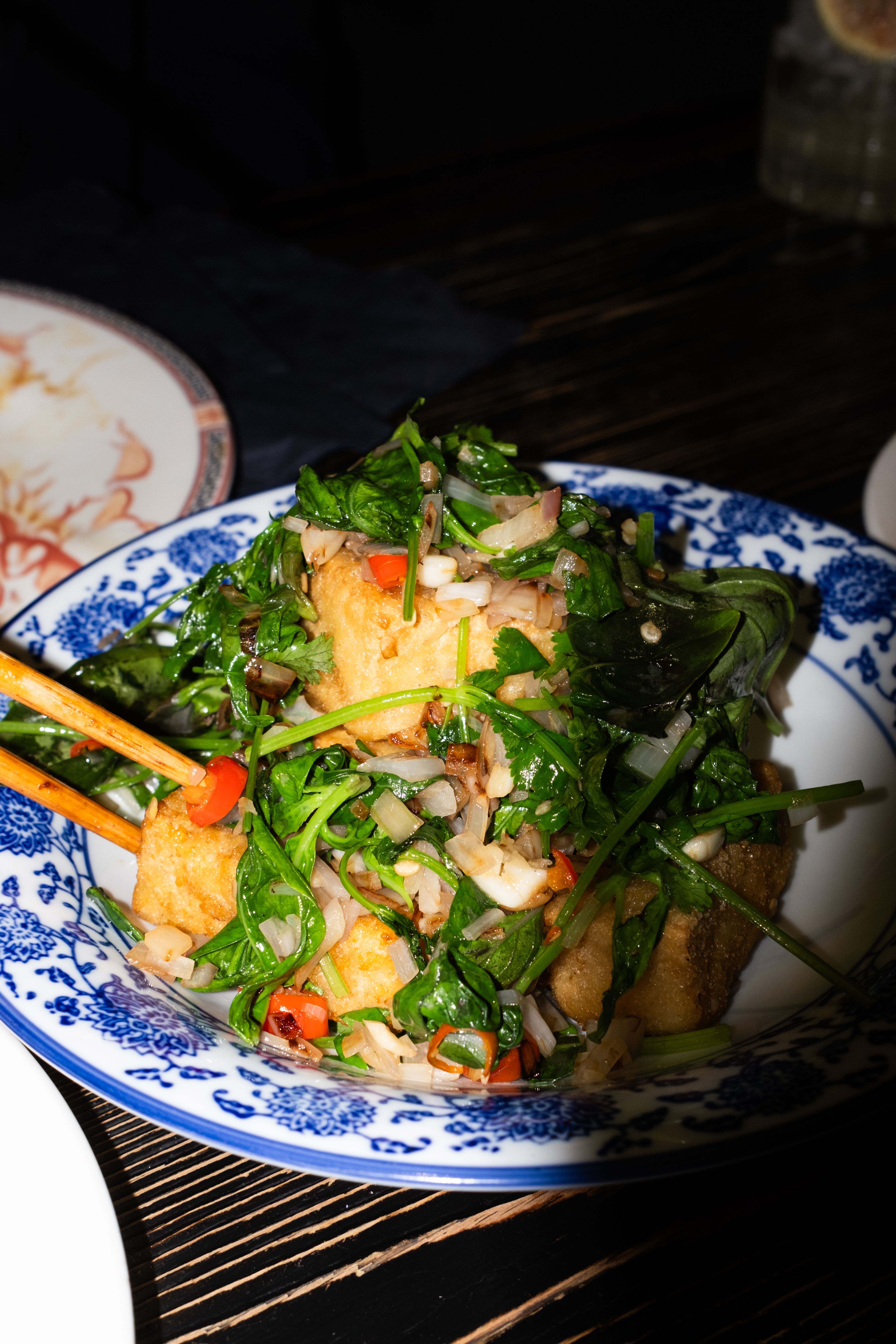 Delicious stir-fried tofu with fresh vegetables served in a traditional Asian blue and white plate.