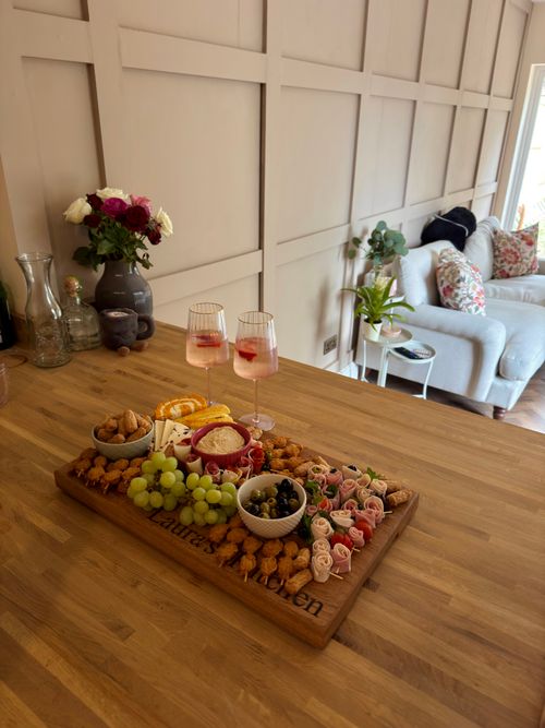 Free Stylish cheese board with grapes, nuts, and drinks on a wooden table in a cozy indoor setting. Stock Photo