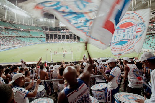 Crowd of enthusiastic fans cheering during a soccer match in a vibrant stadium setting.