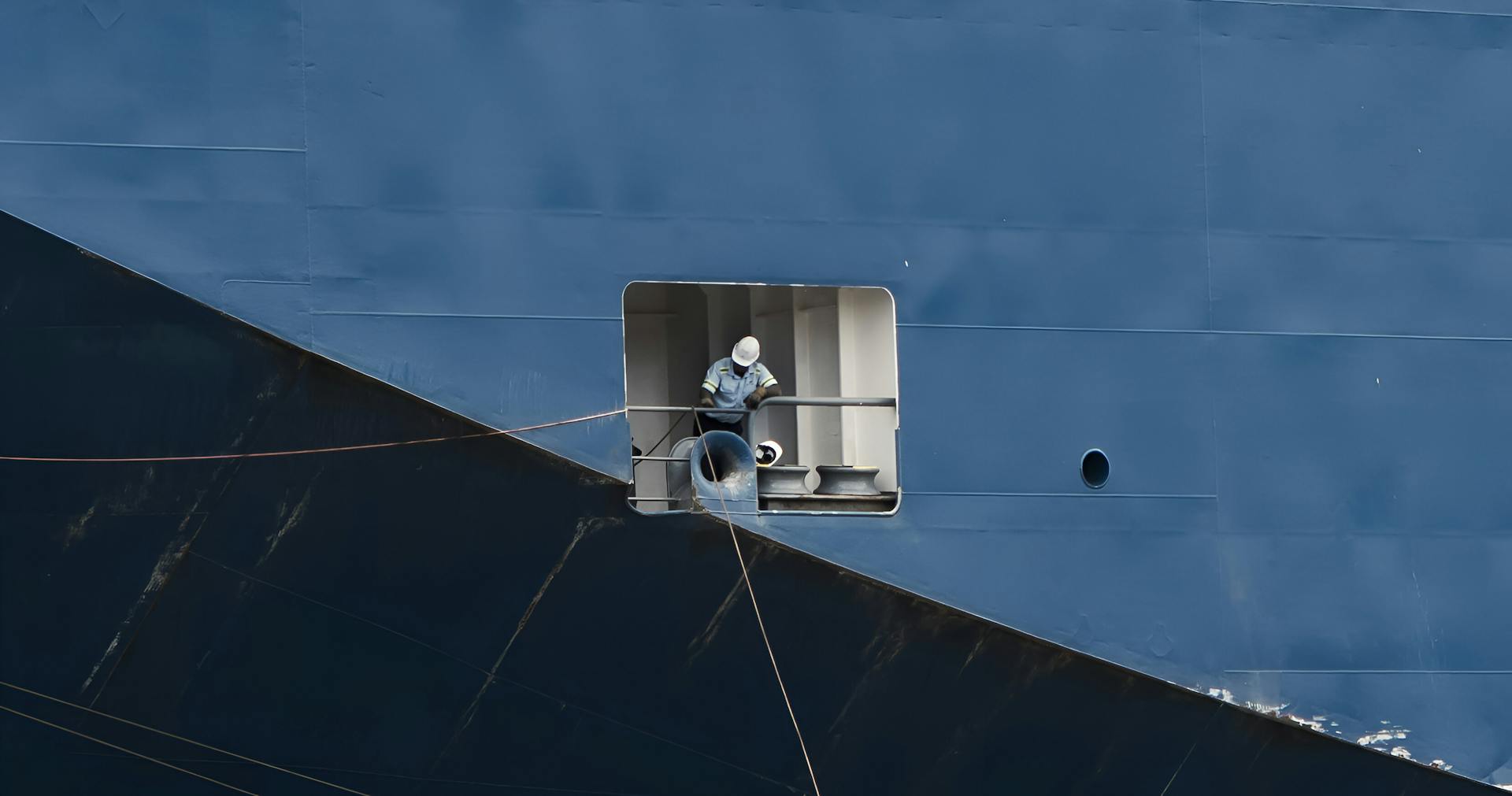 A worker performs maintenance on a large ship's side, highlighting marine industry operations.