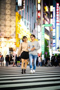 A young couple enjoys a night walk across the vibrant Shibuya Crossing in Tokyo, Japan.