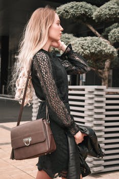 户外的黑色蕾丝连衣裙与皮包旁站着一位时尚的年轻女子