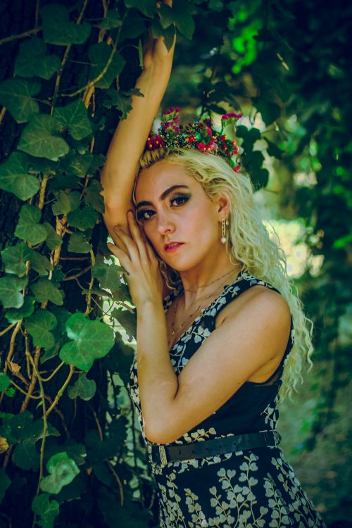 Free Artistic portrait of a blonde woman in nature wearing a floral crown and black dress. Stock Photo