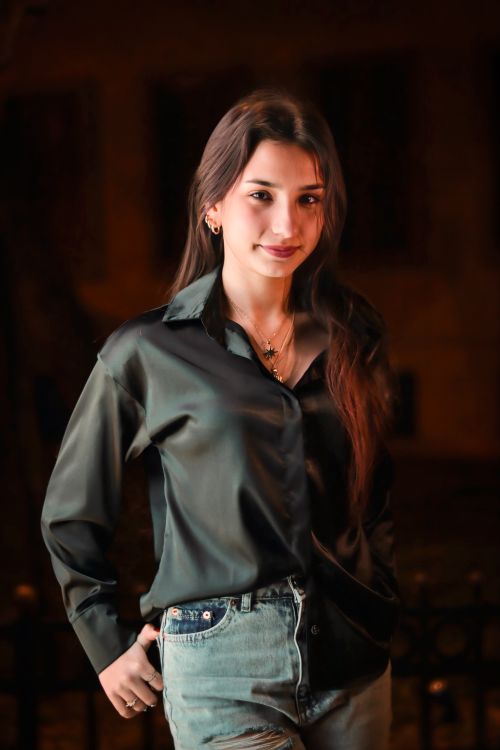Free Portrait of a young woman in a dark shirt and jeans during nighttime setting. Stock Photo