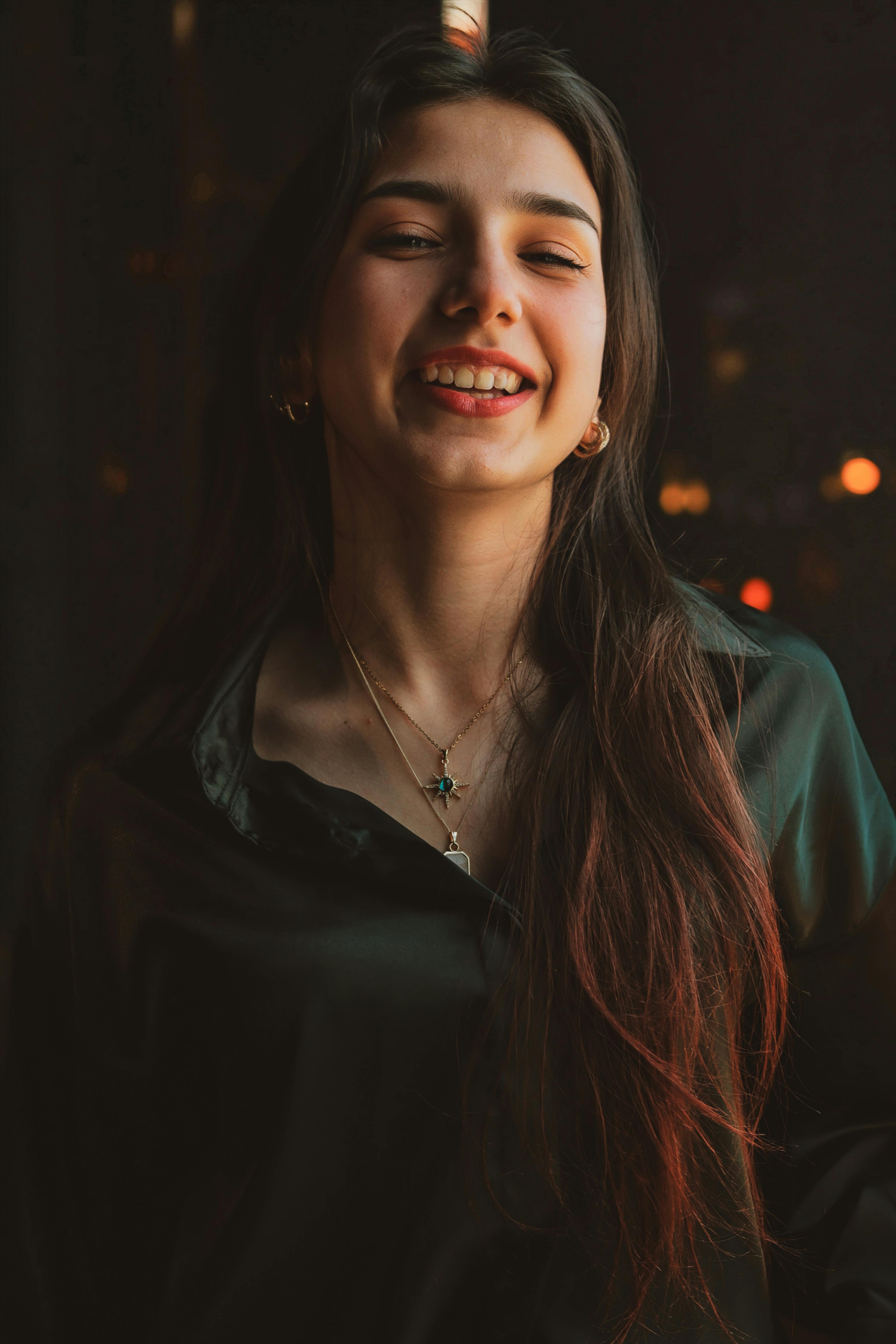 무료 따뜻한 조명이 비치는 어두운 방에서 웃는 젊은 여성의 초상화. 스톡 사진