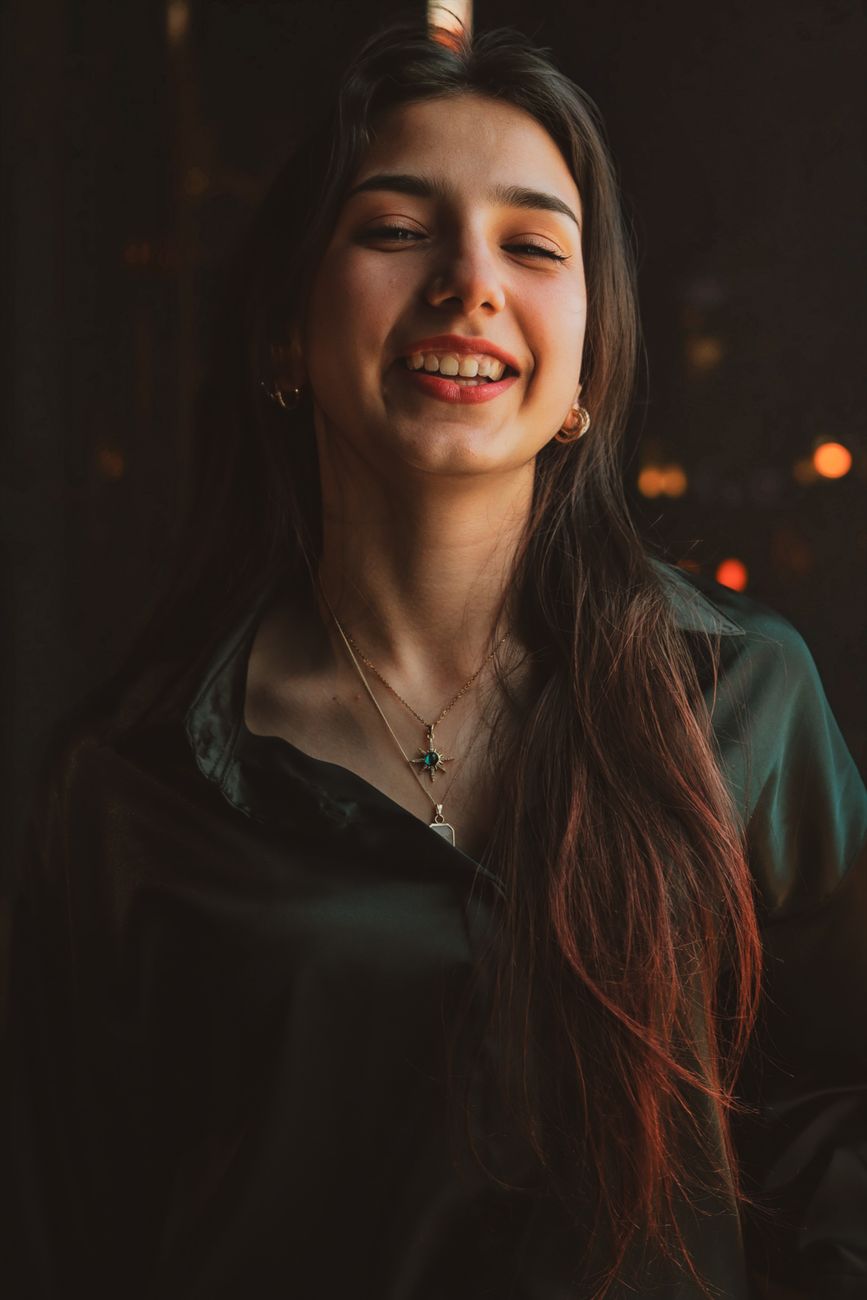 Portrait of a smiling young woman in a dark room with warm lighting.