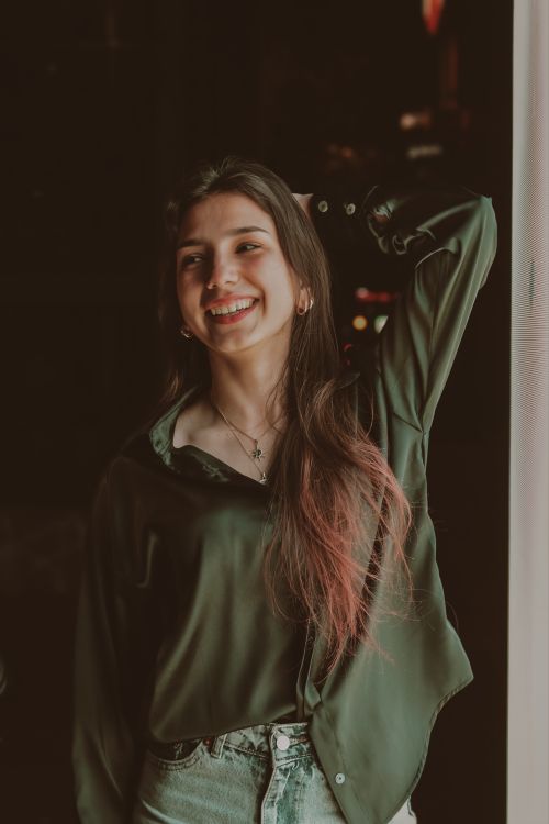 Free A joyful woman wearing a green blouse, smiling and posing indoors near a window. Stock Photo