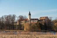Scenic view of a historic castle with trees and a pond in a serene landscape.