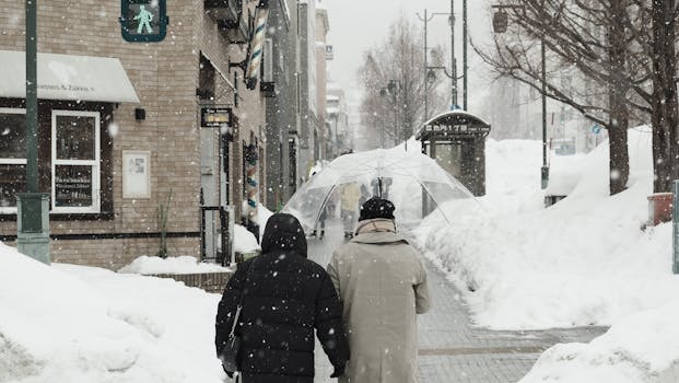 Snowy street scene in Sapporo, Hokkaido, Japan, with people walking under umbrellas.
