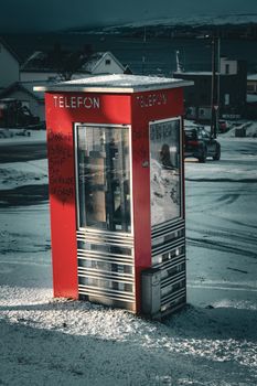 A classic red telephone booth covered in snow on a winter day in Tromsø, Norway.