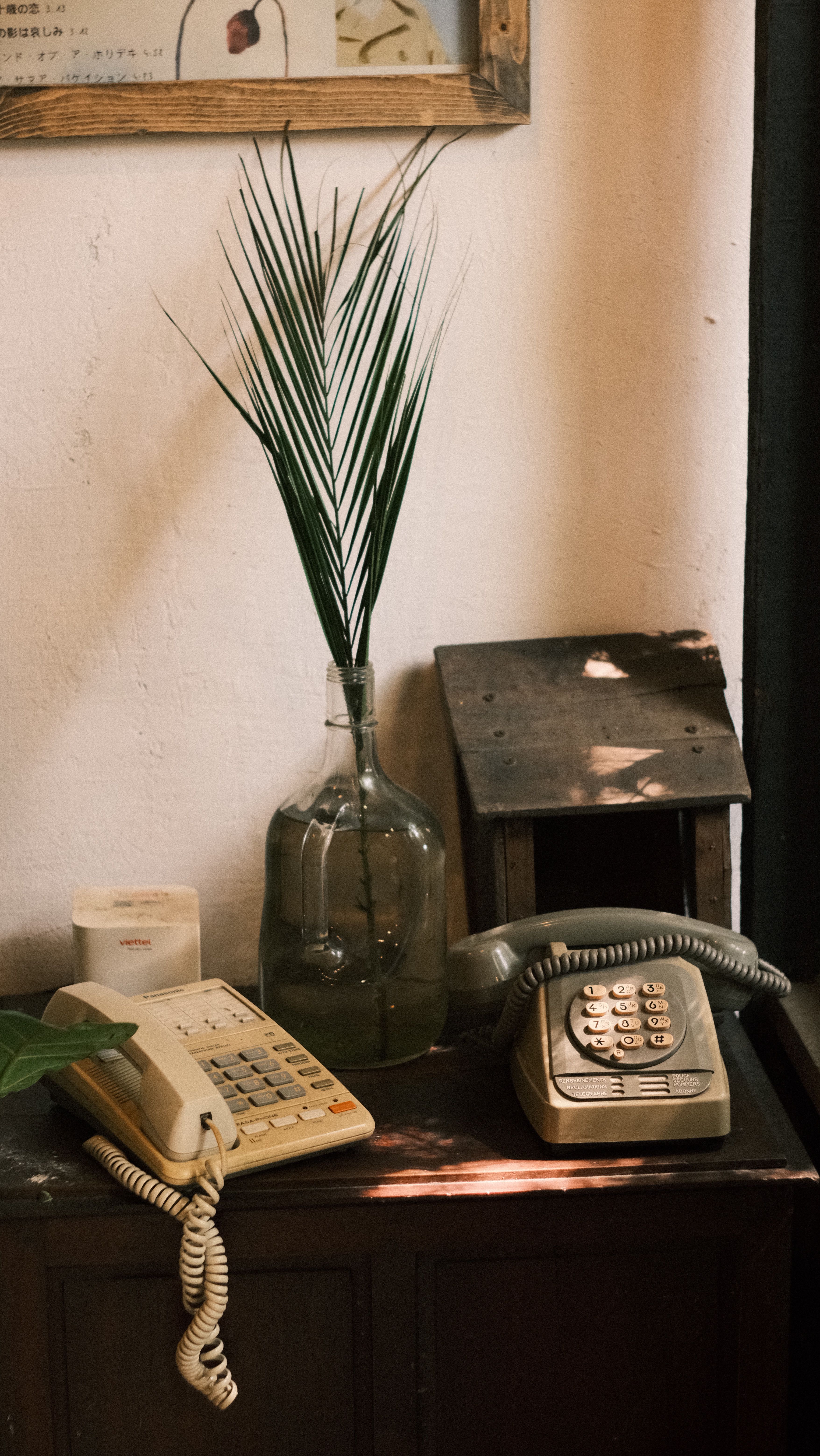 Vintage telephones and jar with leaf on rustic table under soft light, creating a nostalgic feel.
