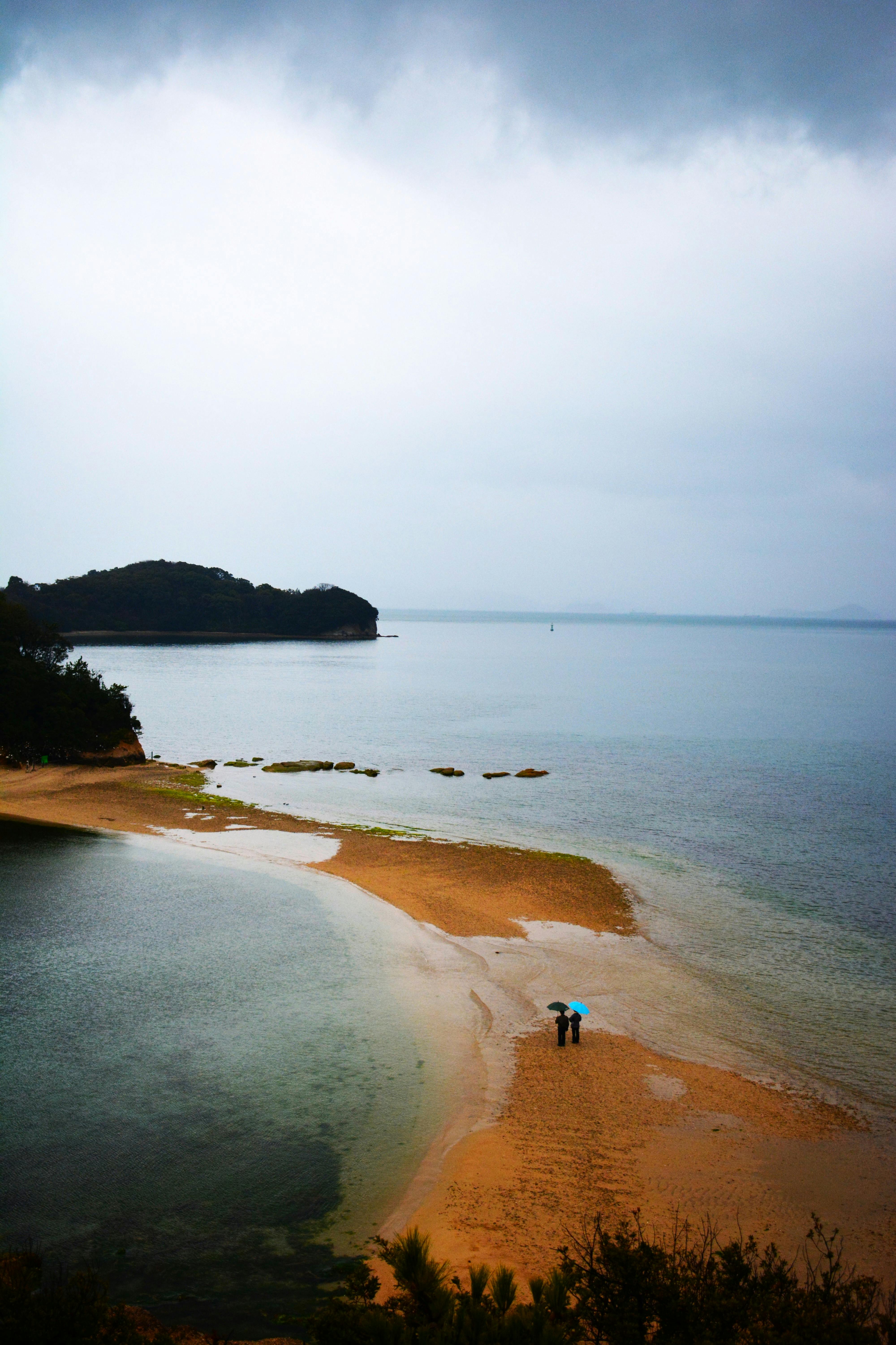 A couple walks on a sandy beach under a cloudy sky, creating a tranquil coastal scene.